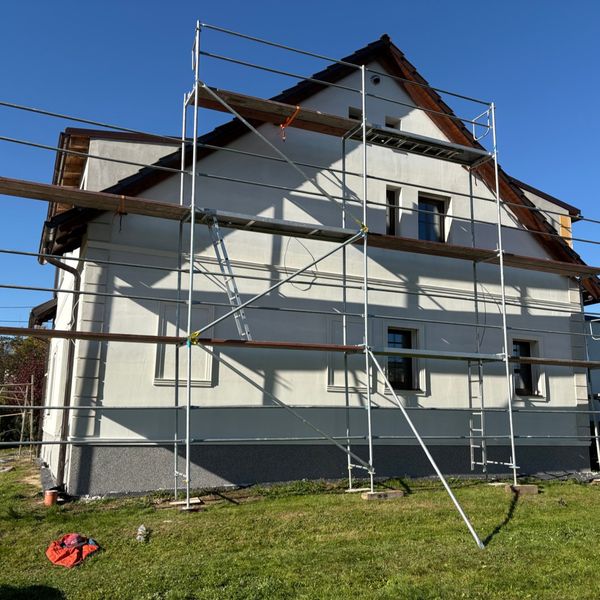 Fasádní lešení kolem patrového rodinného domu se světlou omítkou
