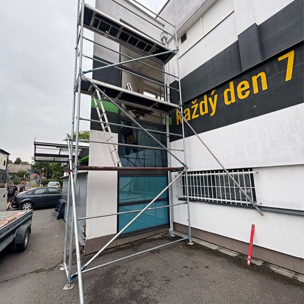 Lešení postavené u vchodu do provozovny v uliční zástavbě