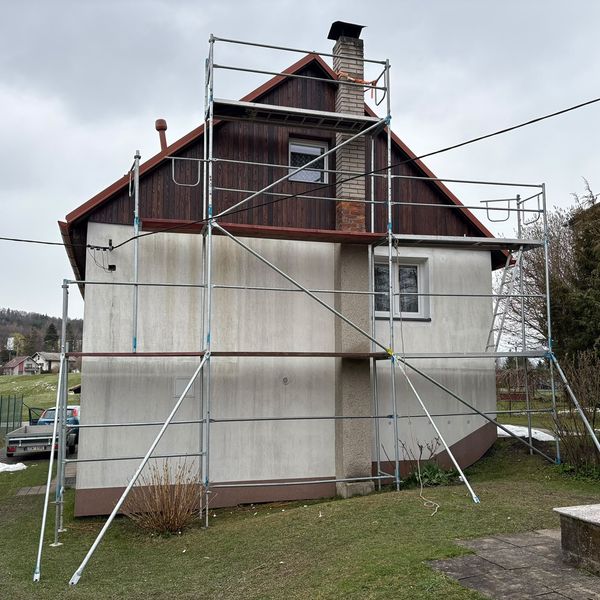 Lešení na domě s dřevěným štítem a světlou fasádou